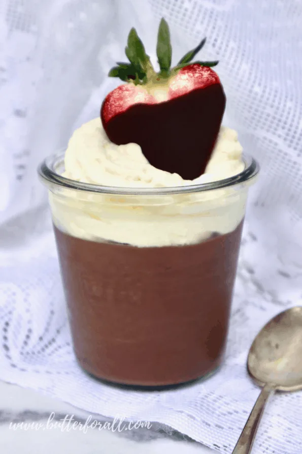 A jar of creamy chocolate pudding with whipped cream and a chocolate-covered strawberry on top. 