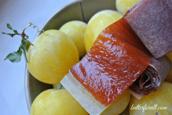 Plum fruit leather resting atop yellow plums in a bowl.