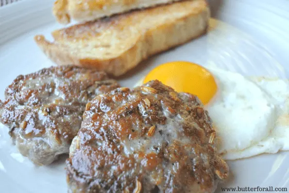 Two freshly cooked sausage patties with a fried egg and toast. 