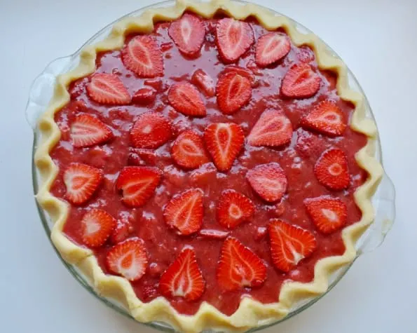 An unbaked strawberry rhubarb pie decorated with fresh strawberry slices. 