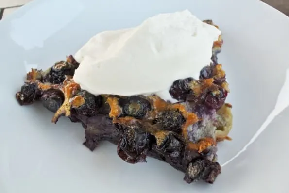 A slice of warm blueberry clafoutis with whipped cream. 