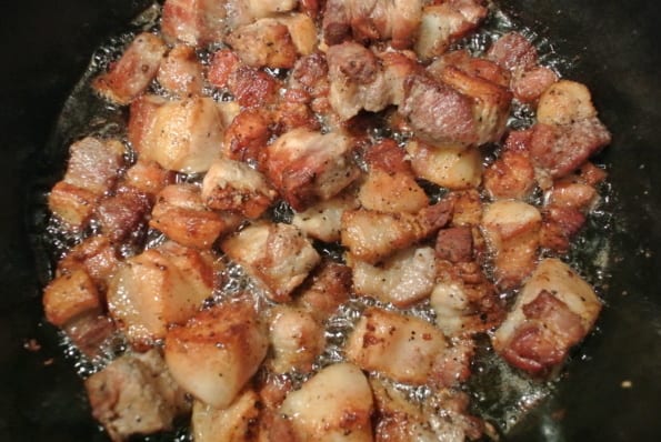 Pieces of pork belly cooking in a pan.
