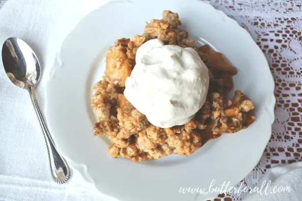 A serving of apple crisp with whipped cream on a plate.