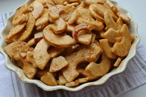 A bowl of thinly sliced apples coated in maple syrup and spices before baking.