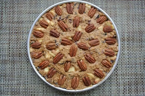 An unbaked fruit and nut cake with pecans arranged on top.