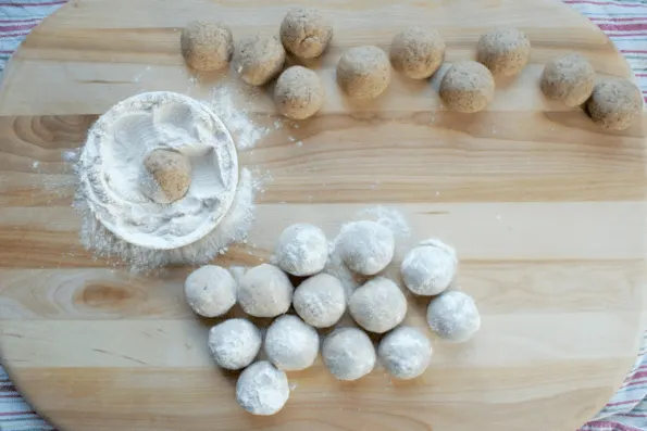 Baked snowball cookies being rolled in maple sugar.
