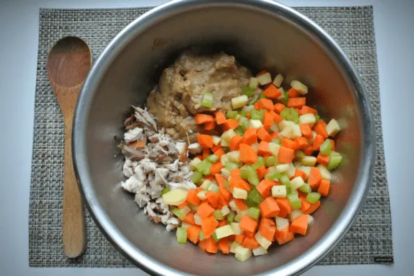 Diced vegetables, gravy, and turkey in a bowl to be mixed.