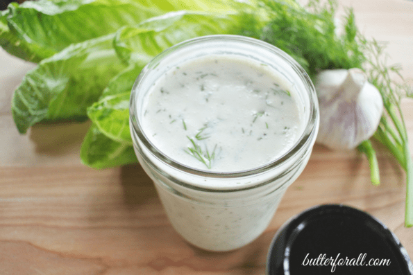 Creamy garlic dill dressing in a jar with lettuce leaves and garlic.