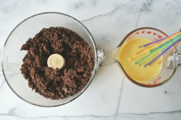 Dry ingredients mixed in a food processor bowl with a cup of wet ingredients ready to add.