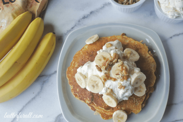 A plate of banana nut sourdough pancakes next to a bunch of bananas.