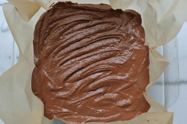 Chocolate coconut butter fudge batter spread onto parchment paper to chill.