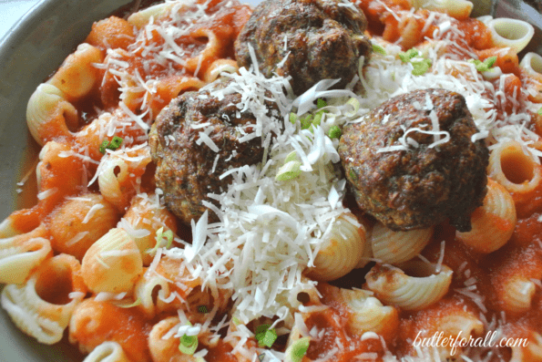 A bowl of pasta and meatballs with grated cheese.