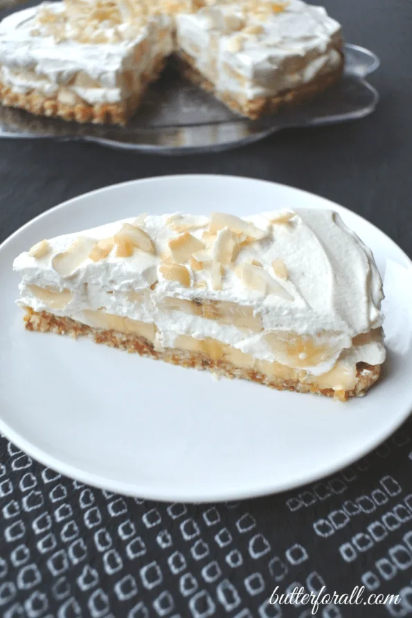 A slice of no-bake banana cream pie on a plate with the whole pie behind it.