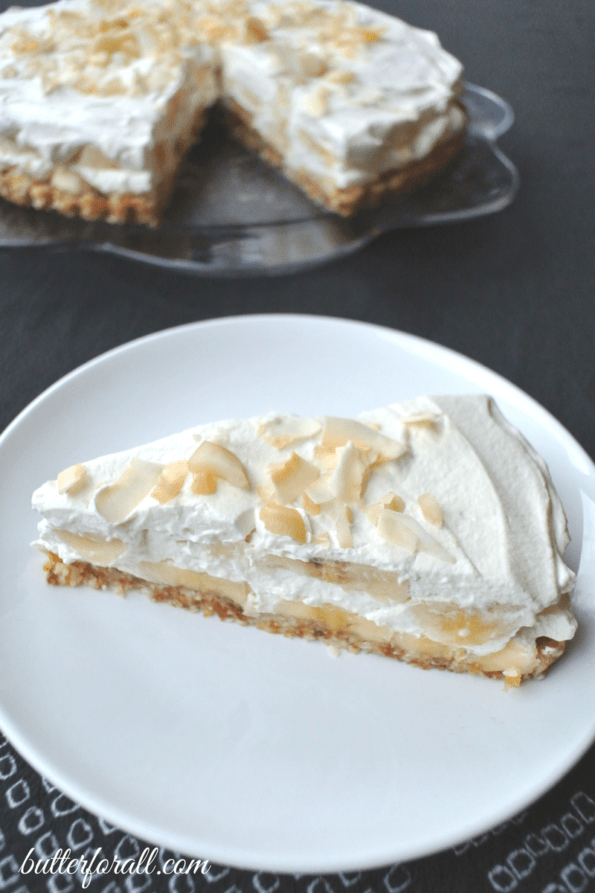 A slice of no-bake banana cream pie on a plate with the whole pie behind it.