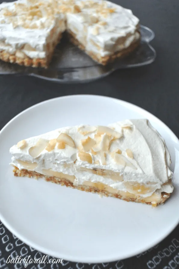 A slice of no-bake banana cream pie on a plate with the whole pie behind it.