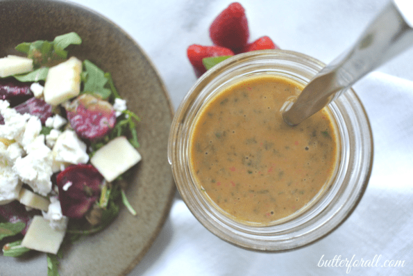 A jar of the prepared vinaigrette next to a plated salad.