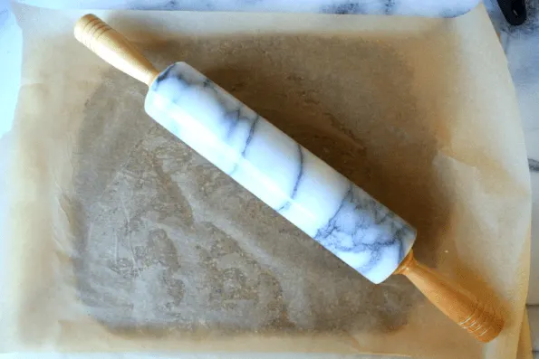 Sesame, cheese, and nut cracker dough being rolled with a rolling pin.
