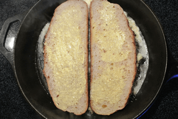 Slices of soaked sourdough frying in a buttered cast-iron pan.