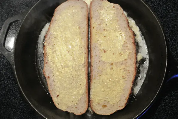 Slices of soaked sourdough frying in a buttered cast-iron pan.