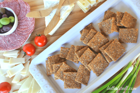 A plate of low-carb sesame, cheese, and nut crackers with cheese and sliced meat.