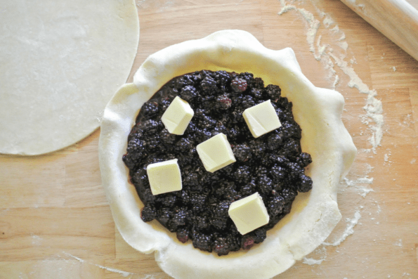 The bottom crust in a pie dish filled with blackberries and dotted with butter.