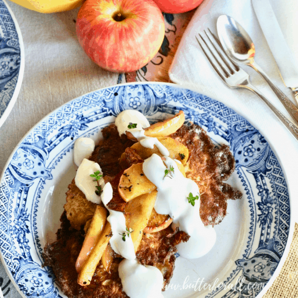 Close up of a beautiful plate of latkes topped with thyme sautéed apples and raw sour cream.