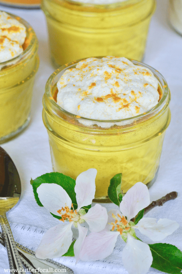 A small glass jar filled with yellow golden milk custard and garnished with whipped cream and a dusting of turmeric.