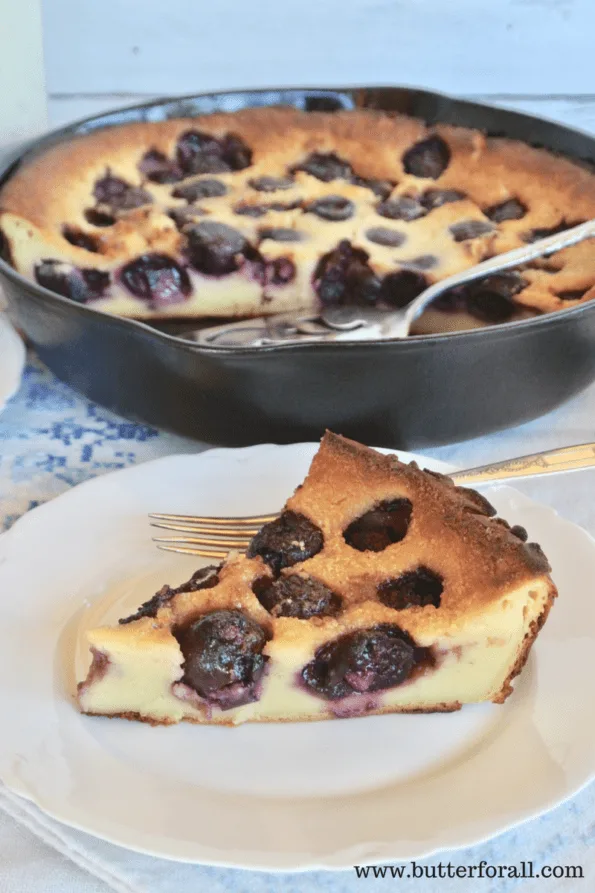 A pan and a slice of sourdough clafoutis fresh out of the oven and bursting with black cherries.