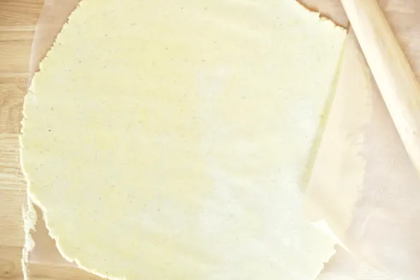 Rolling the sourdough and masa harina cornmeal crust between two pieces of parchment paper.