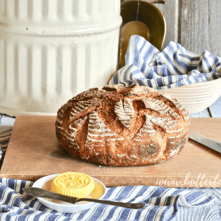 A beautiful loaf of fresh whole grain sourdough sits atop a cutting board just waiting to be cut.