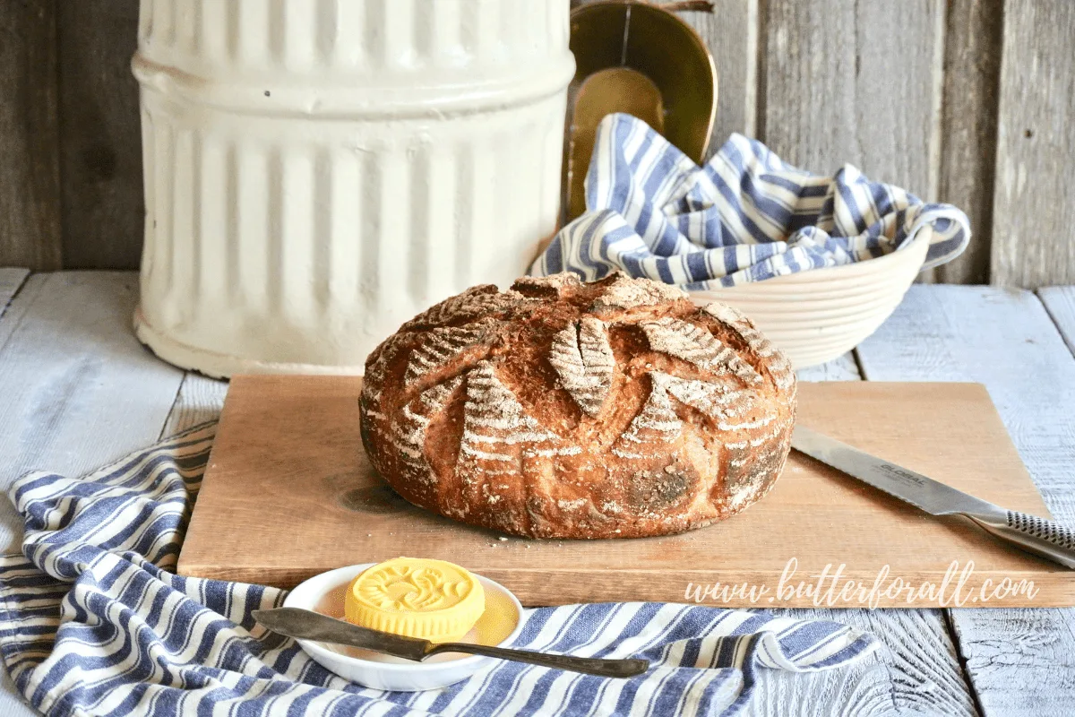 A beautiful loaf of fresh whole grain sourdough sits atop a cutting board just waiting to be cut.