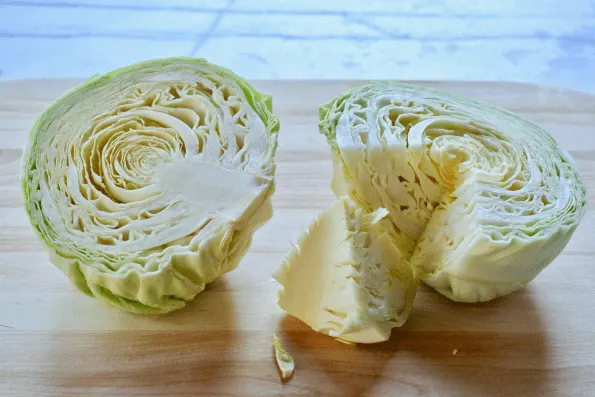 The cabbage head is cut in half and cored.