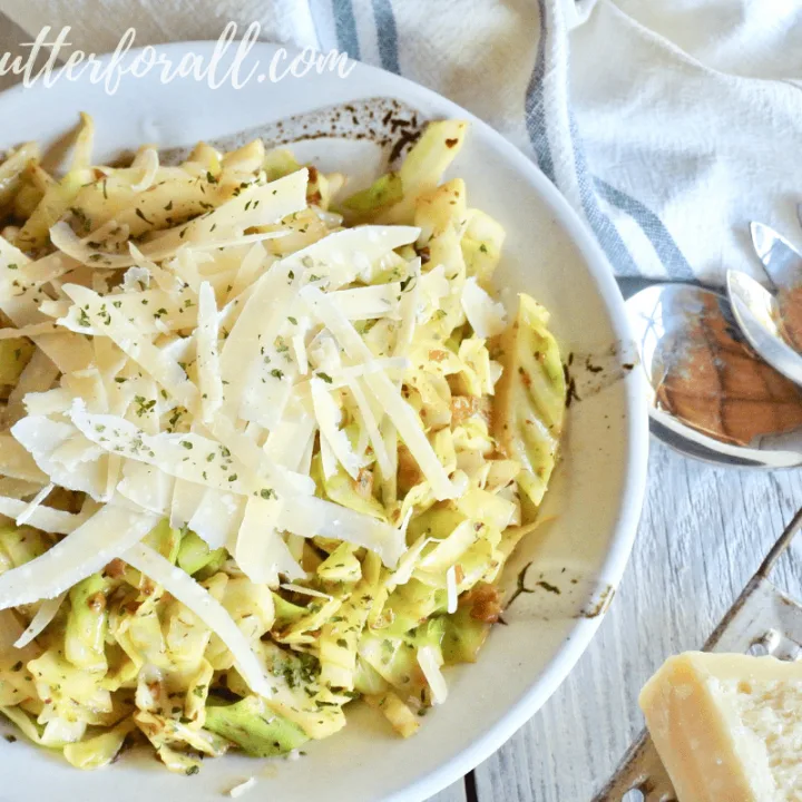 A beautiful bowl of keto friendly cabbage noodles is flavored with extra garlic butter and topped with fresh shaved parmesan cheese.