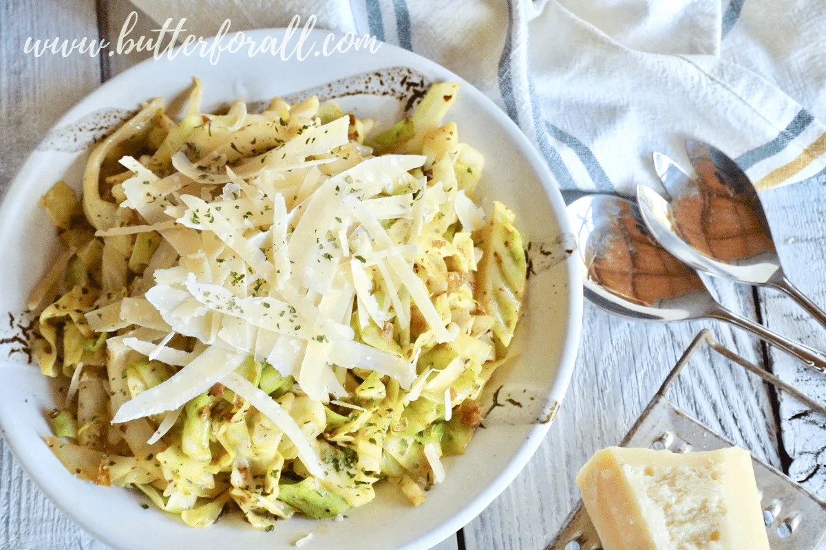 A beautiful bowl of keto friendly cabbage noodles is flavored with extra garlic butter and topped with fresh shaved parmesan cheese.