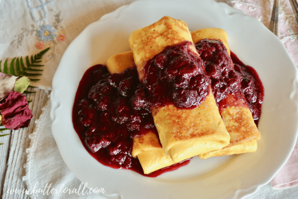 A plate of fresh butter fried blintzes topped with lots of warm berry compote.