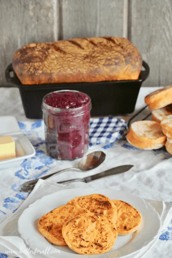 A breakfast spread with fresh sweet potato sourdough English muffins and a bread loaf with fresh butter and homemade jam. 