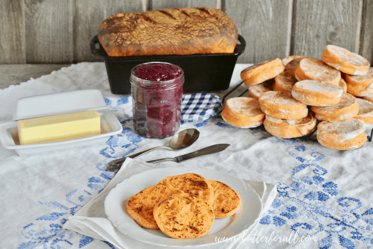 A breakfast buffet featuring a fresh baked loaf of sweet potato sourdough and soft and chewy sweet potato English muffins with jam and butter.