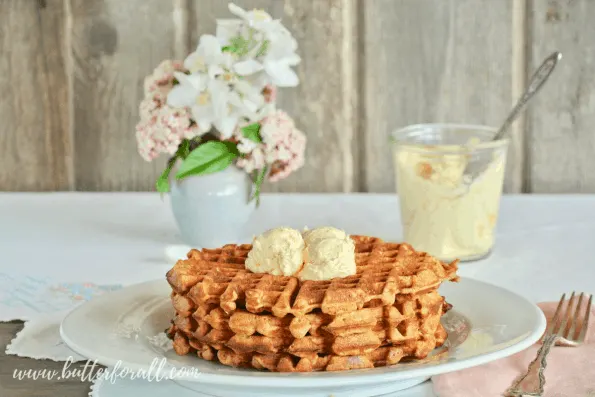 A table set with carrot cake waffles with honey butter frosting and fresh flowers. 