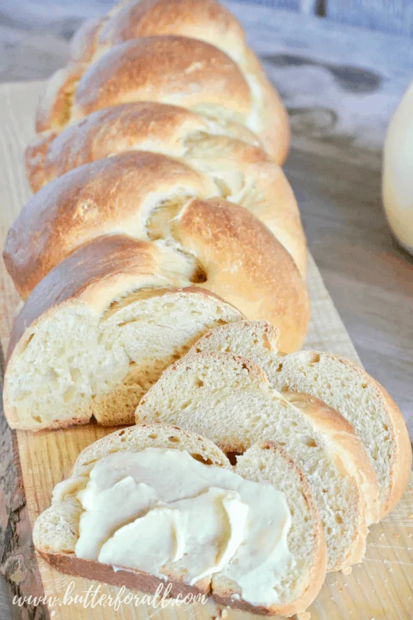 A braided sourdough challah sliced and slathered with butter.