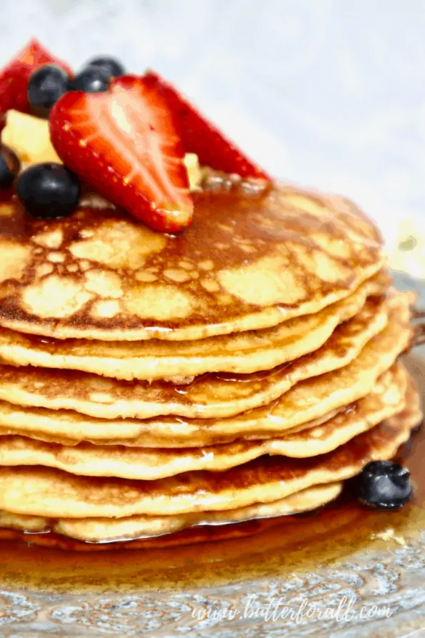 A close-up of a stack of sourdough pancakes with syrup and fresh berries.