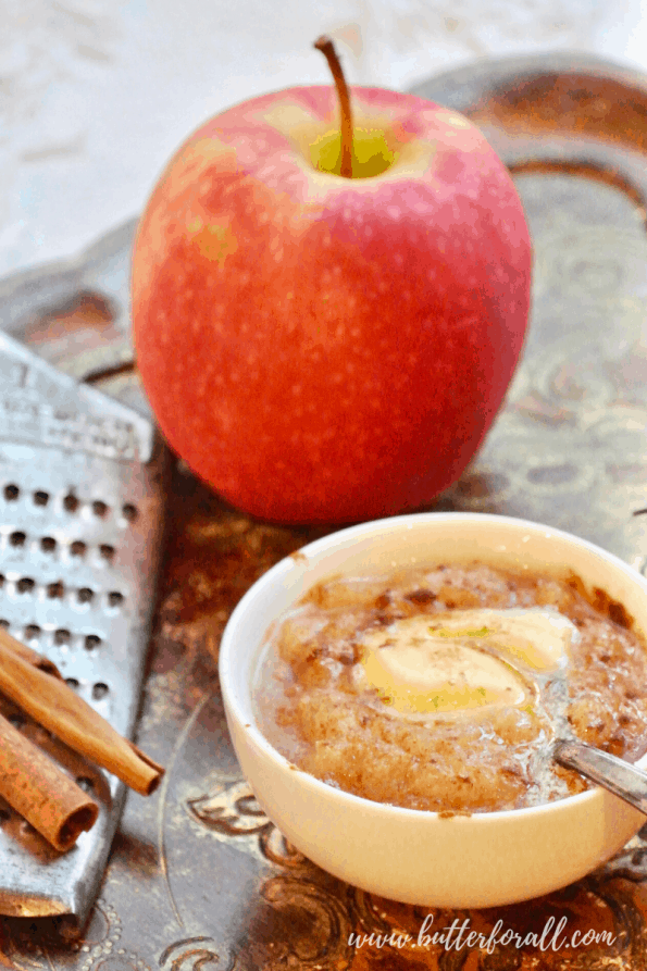 A bowl of hot buttery apple sauce and an apple.