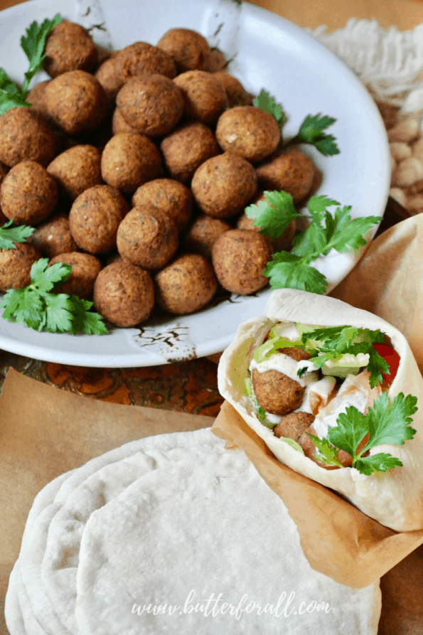 A pita stuffed with fried falafel balls, tahini, and veggies next to a bowl of falafel balls.