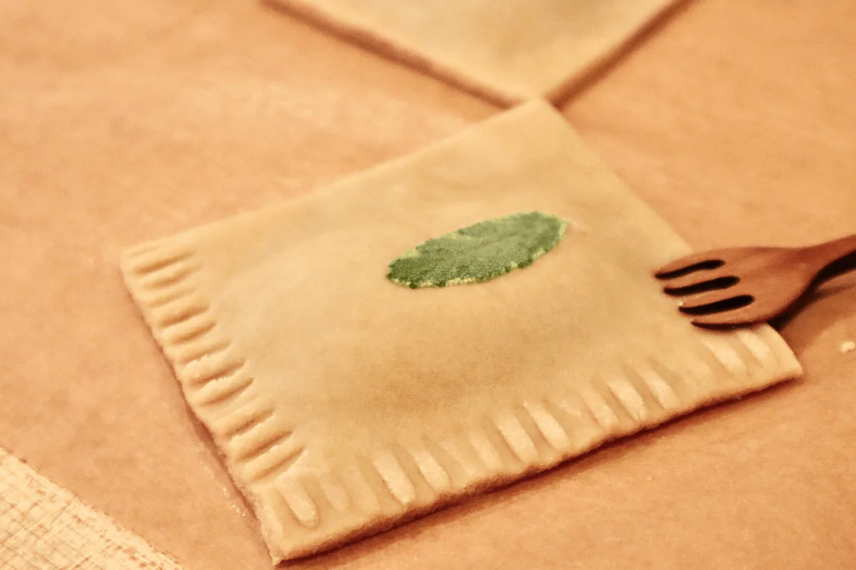 A raw pastry square being crimped around each edge with a fork.