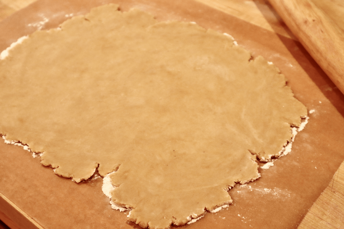 Dough rolled out on parchment paper with jagged edges.