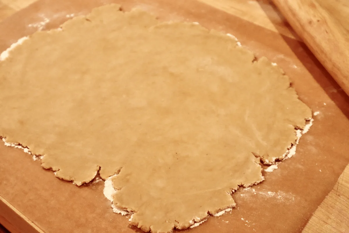 Dough rolled out on parchment paper with jagged edges.