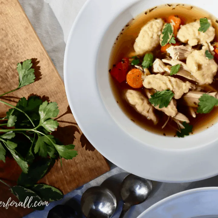 A bowl of Chicken and Sourdough Dumplings garnished with fresh parsley and sage.