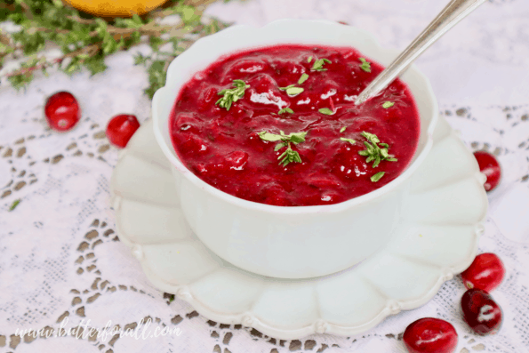 A bowl of bright red fresh cranberry sauce garnished with sprigs of fresh thyme.