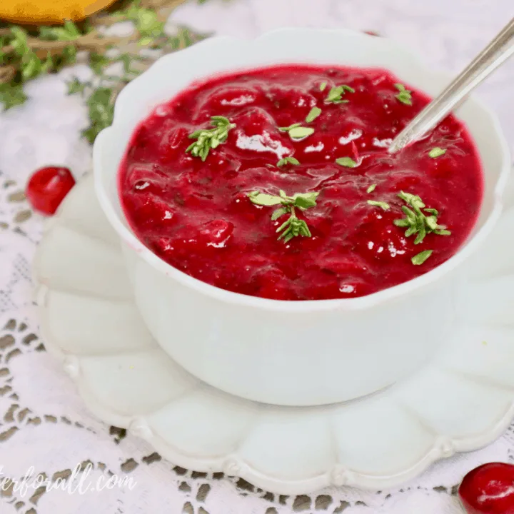 A bowl of bright red fresh cranberry sauce garnished with sprigs of fresh thyme.