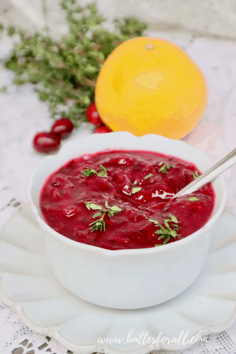 A bowl of bright red fresh cranberry sauce garnished with sprigs of fresh thyme.