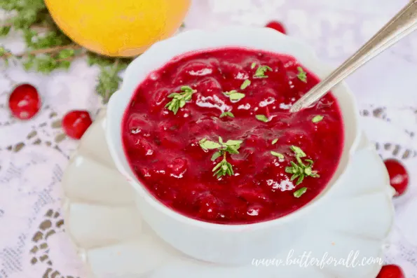 A bowl of bright red fresh cranberry sauce garnished with sprigs of fresh thyme.